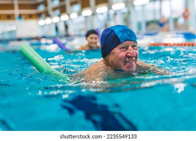 Portrait of smiling happy positive white senior adult man with blue swimming swim cap on his head using foam green pool noodle. Indoor shot. Sports area. High quality photo - Powered by Shutterstock