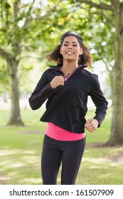 Portrait Of A Smiling Healthy Young Woman In Black Jacket Jogging In The Park