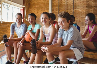 Portrait Of Smiling High School Kids Sitting On Bench In Basketball Court