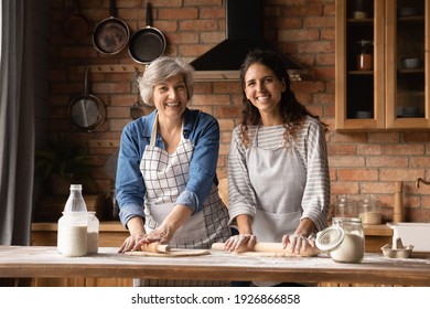 Portrait Of Smiling Hispanic Elderly Mom And Grownup Daughter Cook Together At Home Kitchen. Happy Adult Millennial Woman And Senior Mother Have Fun Baking Cookies Pie. Family Hobby Concept.