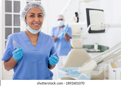 Portrait Of Smiling Hispanic Woman Dentist Preparing Tools At Modern Dental Office..