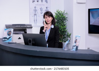 Portrait of smiling hospital receptionist answering call from patient to make an appointment for clinical consult at private clinic. Professional looking woman working at front desk using telephone. - Powered by Shutterstock