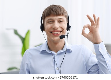 Portrait of smiling hotline operator in headset showing ok gesture in office