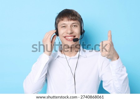 Portrait of smiling hotline operator in headset showing thumbs up on light blue background