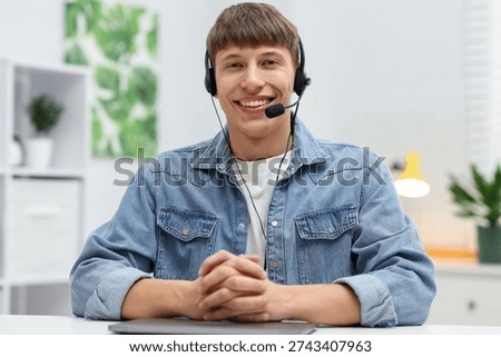 Portrait of smiling hotline operator in headset at table in office