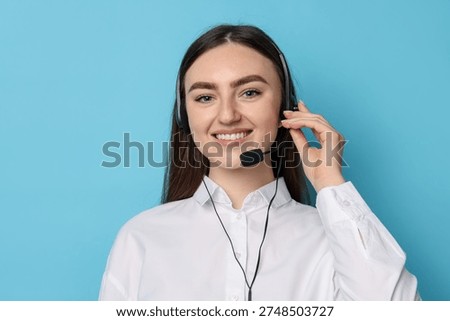 Portrait of smiling hotline operator in headset on light blue background