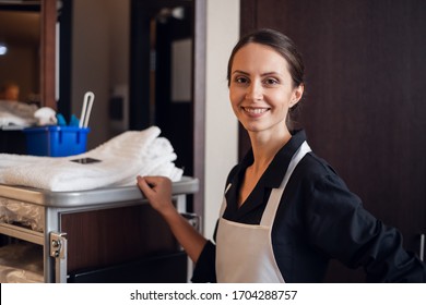 A portrait of a smiling housekeeping lady with a cart