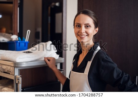 A portrait of a smiling housekeeping lady with a cart