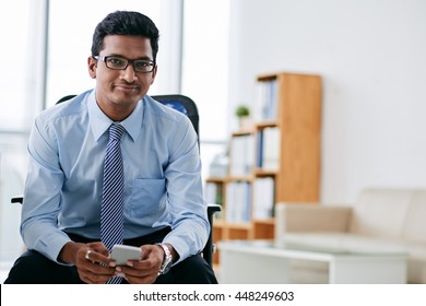 Portrait of smiling Indian business person with smartphone sitting in office