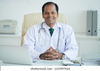 Portrait Of Smiling Indian Male Doctor Sitting At His Workplace