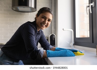 Portrait smiling Indian woman housewife wearing rubber gloves washing kitchen, cleaning table surface at home, happy young housekeeper looking at camera, wiping dust with napkin, housekeeping - Powered by Shutterstock