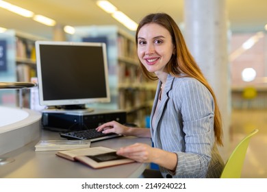 Portrait Of Smiling Intelligent Young Woman Reading Textbooks While Studying In Public Library Computer Room..