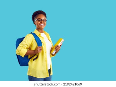 Portrait of smiling international female student with backpack and textbooks on light blue background. Happy african american girl in casual clothes and glasses looking proudly at camera. - Powered by Shutterstock