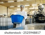 Portrait of smiling interracial foreign blue collar worker carrying plastic container near food processing machine.