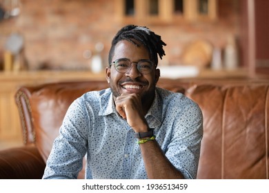 Portrait Of Smiling Joyful Young Black Male Hipster Sitting On Sofa Looking At Digital Camera Making Video Call From Home. Positive Afro American Man Student Participate In Online Event Web Conference