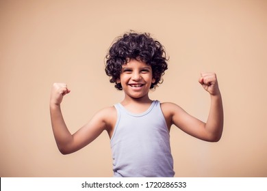 A Portrait Of Smiling Kid Boy With Curly Hair Showing Strong Of Hands. Children And Health Concept