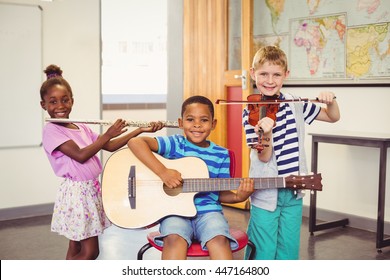 Portrait of smiling kids playing guitar, violin, flute in classroom at school