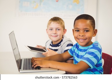 Portrait Of Smiling Kids Using A Laptop And Digital Tablet In Classroom At School