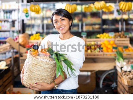 Portrait of smiling latin american woman with wicker basket with fresh grocery, enjoying shopping in store