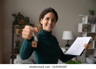 Portrait Of Smiling Latin Female Real Estate Agent Show Home Keys Consider Architectural Plan. Happy Hispanic Realtor Or Broker Offer Suggest Good House Or Apartment Sale Deal. Rent, Mortgage Concept.