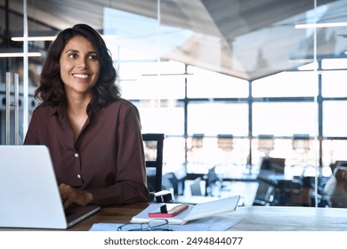 Portrait of smiling latin hispanic middle-aged business woman work on laptop computer in modern office. Indian young businesswoman professional employee using pc, looking dreaming aside. Copy space - Powered by Shutterstock