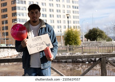 Portrait Of A Smiling Latino Man With A Happy Valentine's Day Sign,gift And Love Balloon Waiting For His Partner To Surprise Him And Celebrate Valentine's Day.