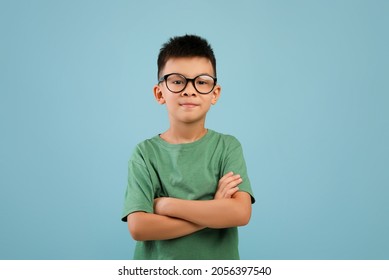 Portrait Of Smiling Little Asian Boy Wearing Eyeglasses Standing With Folded Arms And Looking At Camera, Confident Nerdy Korean Male Child Posing Over Blue Studio Background, Copy Space