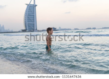 Portrait smiling little baby boy playing in the sea, ocean. Positive human emotions, feelings, joy. Funny cute child making vacations and enjoying summer. Sunset Dubai beach.