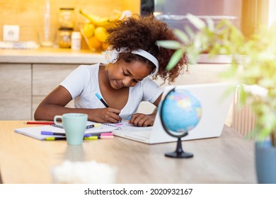 Portrait of smiling little biracial girl in headphones do homework study online in kitchen, happy small African American child in earphones have online web class or lesson using laptop at home - Powered by Shutterstock
