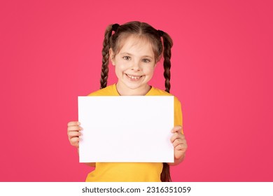 Portrait Of Smiling Little Girl Holding Blank White Placard In Hands, Happy Preteen Female Kid Demonstrating Copy Space For Your Text Or Design, Showing Empty Board, Standing Over Pink Background - Powered by Shutterstock