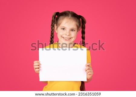 Portrait Of Smiling Little Girl Holding Blank White Placard In Hands, Happy Preteen Female Kid Demonstrating Copy Space For Your Text Or Design, Showing Empty Board, Standing Over Pink Background