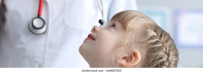 Portrait Of Smiling Little Girl At Pediatrist. Cheerful Child Looking Up At Doctor In Medical Gown And Stethoscope With Gladness. Medicine And Healthcare Concept