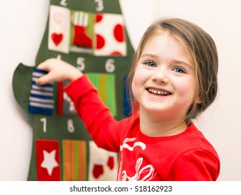 Portrait Of A Smiling Little Girl Putting Her Hand Into Pocket Of Advent Christmas Calendar