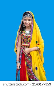 Portrait of smiling little indian girl kid wearing traditional colorful rajasthani outfit and jewelery against blue background.