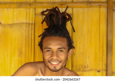 portrait of smiling local guy man with dreadlocks with wooden in the background.