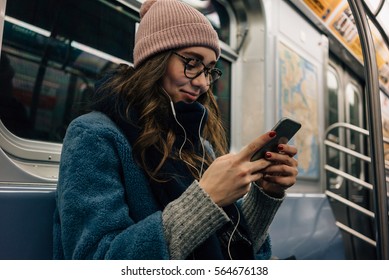 Portrait of a smiling lovely girl typing message on mobile phone in subway train
