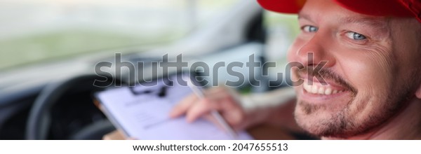 Portrait of smiling male courier driver in car\
salon with documents