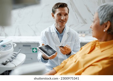 Portrait of smiling male dentist holding digital tablet with teeth x-ray image while explaining dental surgery to patient - Powered by Shutterstock