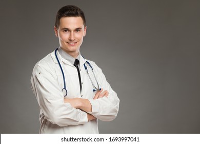 Portrait Of A Smiling Male Doctor With Arms Crossed. Waist Up Studio Shot On Gray Background.