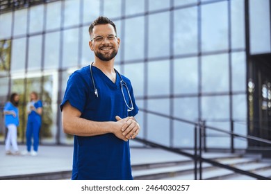 Portrait of smiling male nurse standing in hospital. Portrait Of Male Doctor Wearing Scrubs Standing In Modern Hospital Building. Male healthcare worker smiling outside, portrait - Powered by Shutterstock