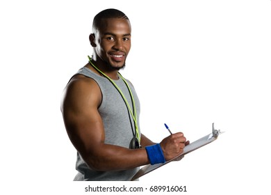 Portrait of smiling male rugby coach writing on clipboard while standing against white background - Powered by Shutterstock