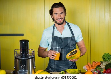 Portrait of smiling male staff holding glass of juice and papaya in health grocery shop - Powered by Shutterstock