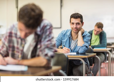 Portrait of a smiling male student with others writing notes in the classroom