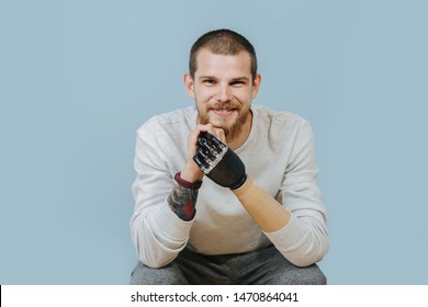 Portrait Of a smiling Man With Artificial hand in casual clothes sitting at the chair and looking at the camera. Studio shot. Isolated blue background