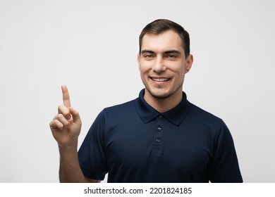 portrait of smiling man in blue T-shirt with finger points up on white background for advertising, mockup
