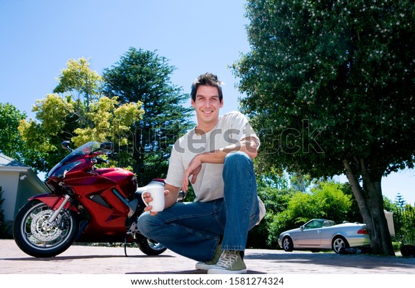 Portrait of\
smiling man with coffee by\
motorbike