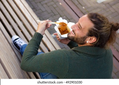 Portrait Of Smiling Man Eating Chinese Food With Chopsticks On Bench