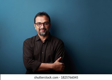 Portrait Of A Smiling Man Of Indian Ethnicity Against A Blue Wall Background.