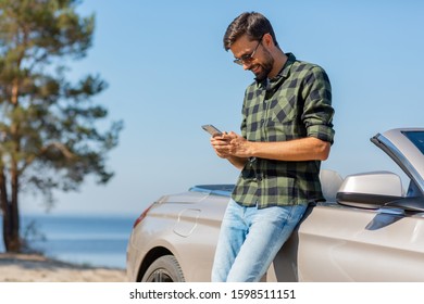 Portrait Of Smiling Man Looking At The Phone Outdoors At Daytime