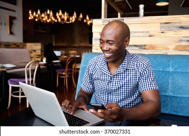 Portrait of smiling man with a mobile phone sitting at cafe using laptop - Powered by Shutterstock